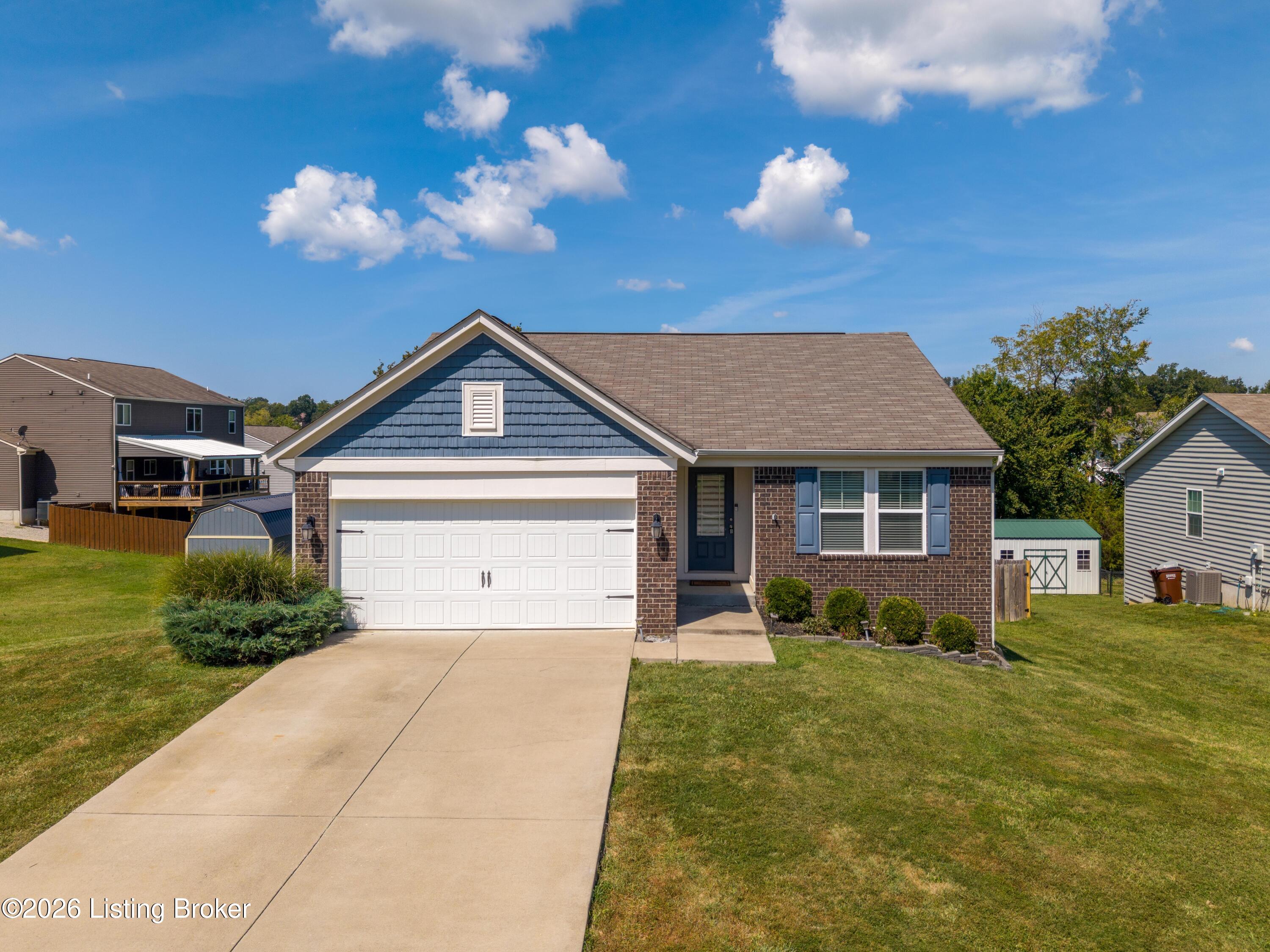 Single-story brick home with a blue gable, white double garage, and broad concrete driveway.