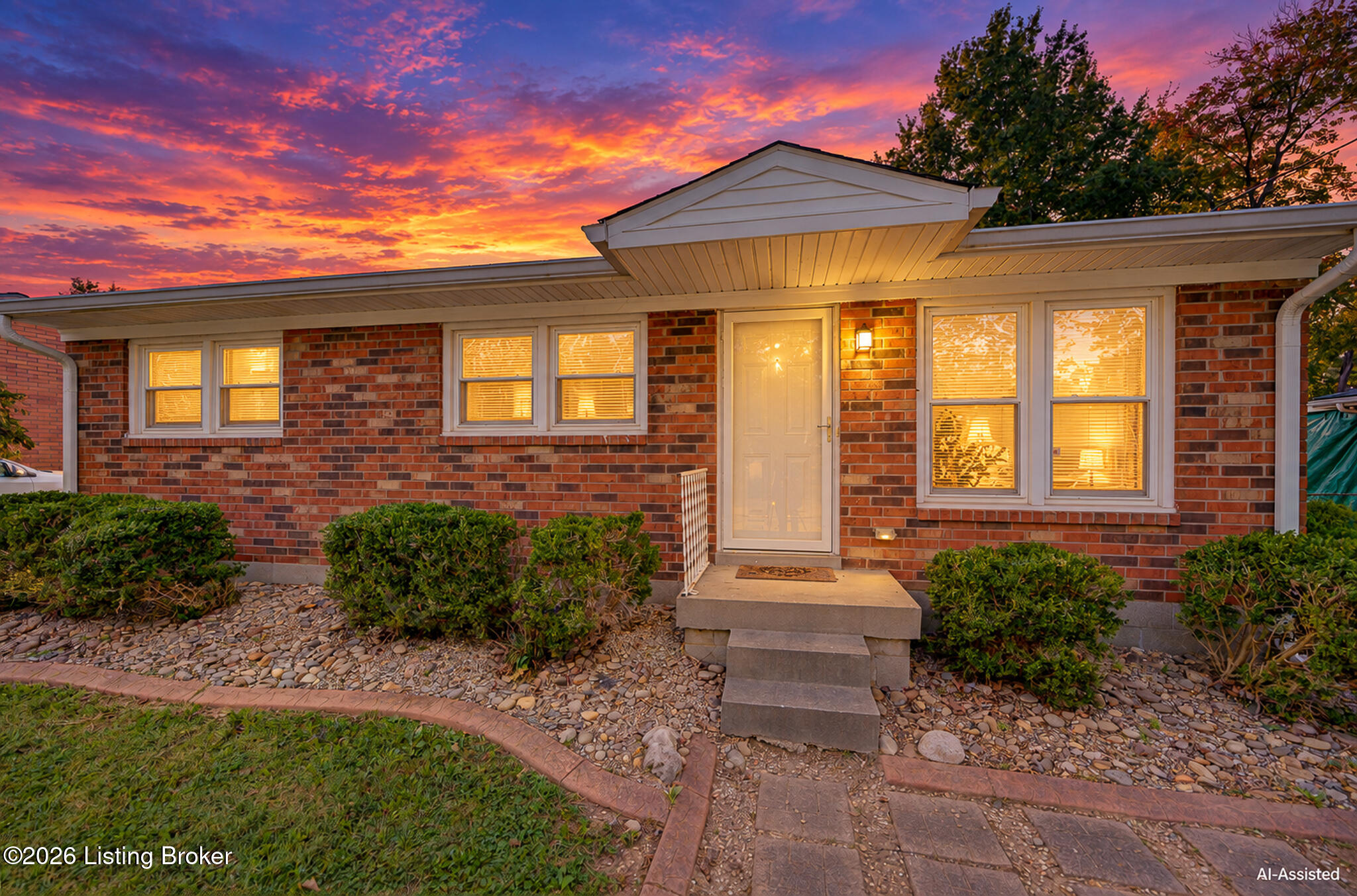 Single-story brick home with illuminated windows and entry beneath a vivid sunset sky.