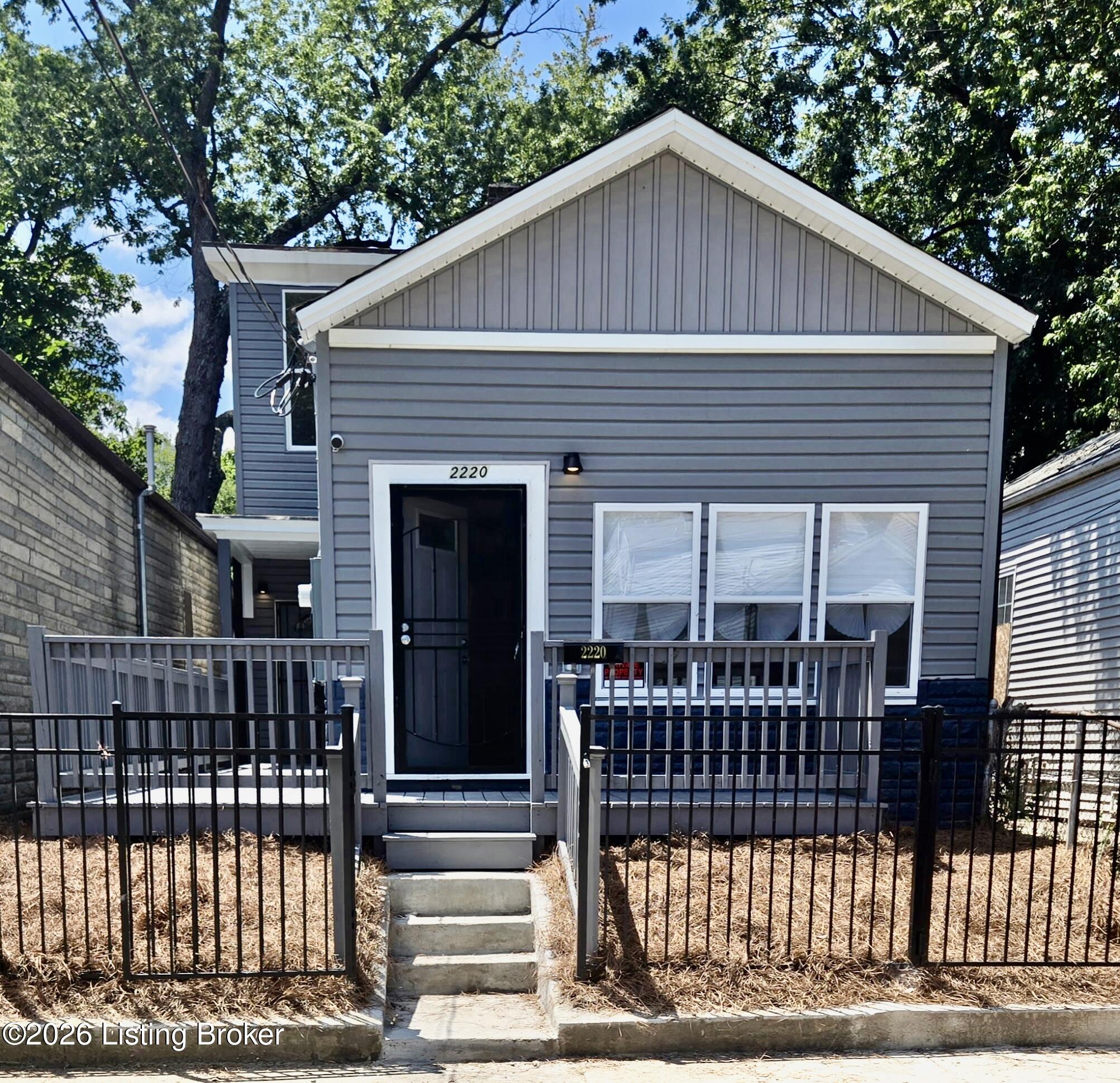 Gray-sided house with a white-trimmed gable, front porch, and fenced yard.