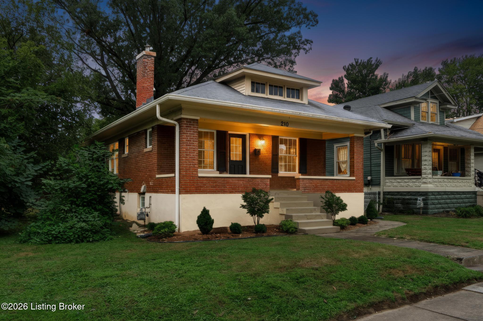 Brick home with a covered front porch and illuminated windows at dusk.