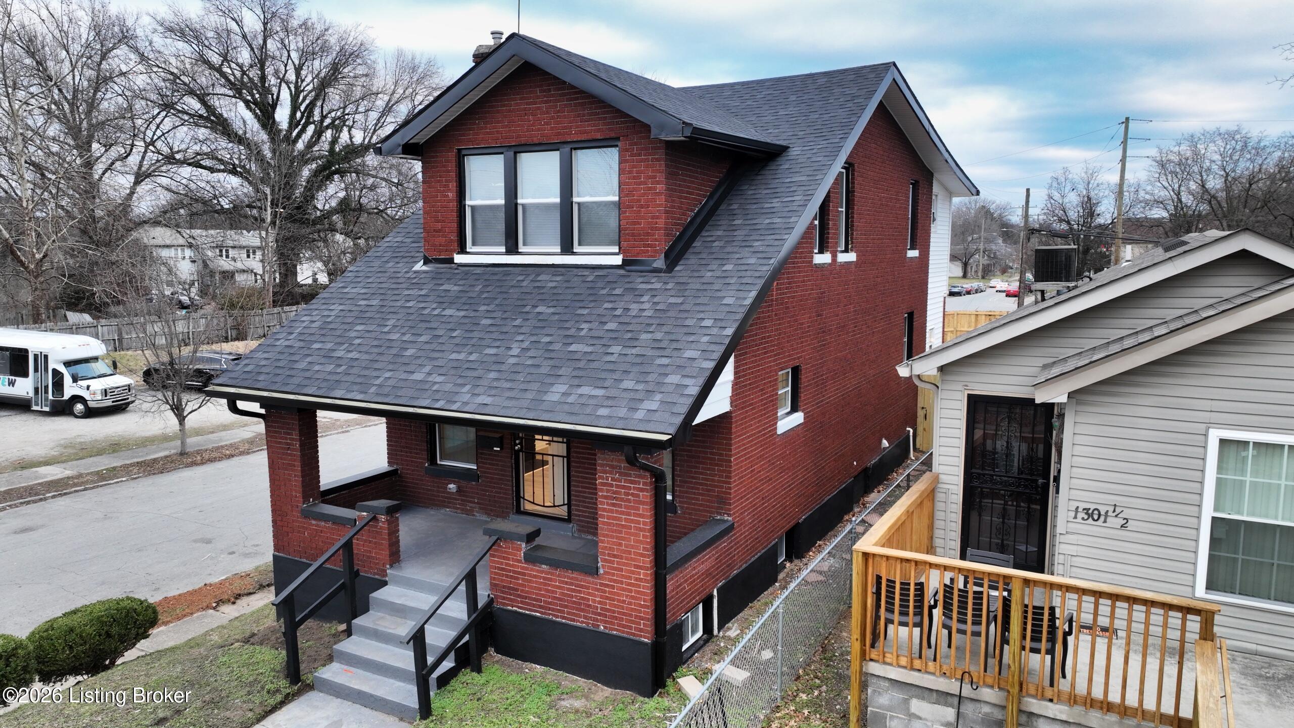 Red brick two-story house with a steep gray roof, front porch, and neighboring homes.