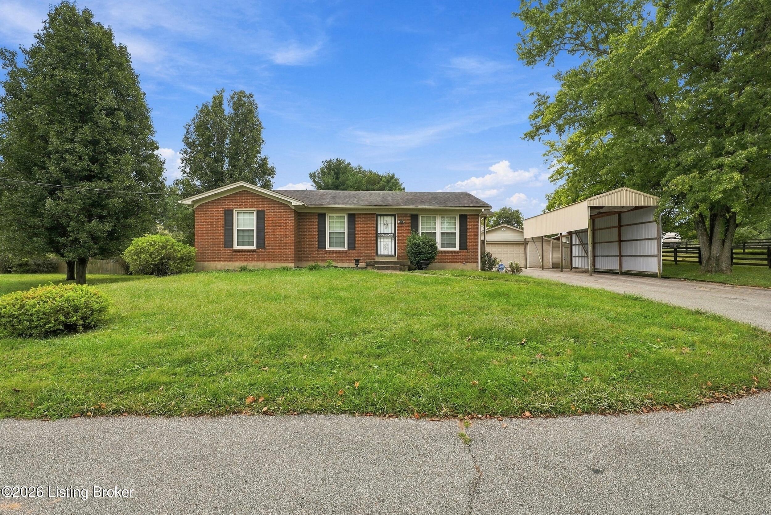 Red brick ranch house with dark shutters, a green lawn, and a metal carport.