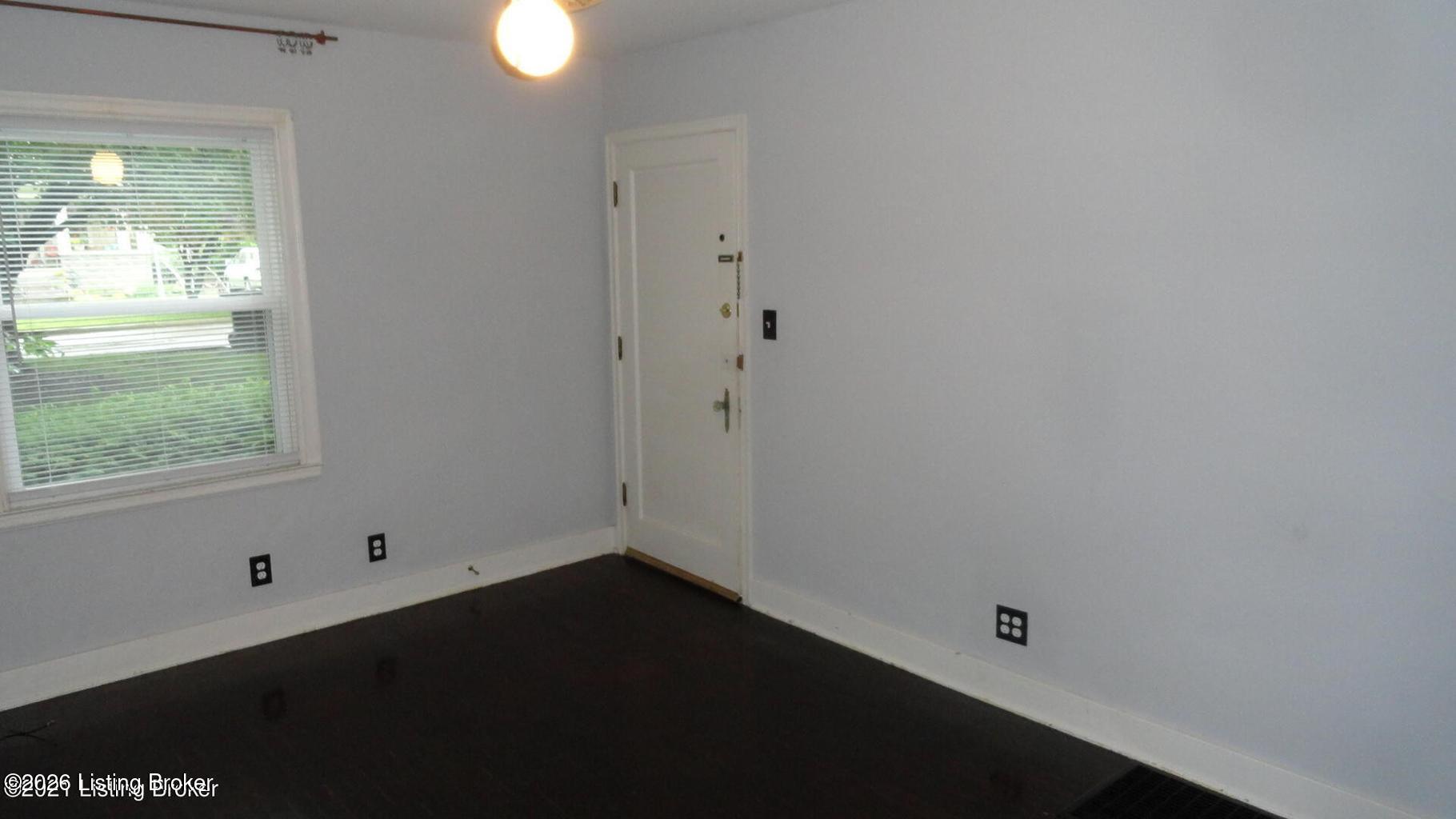 Vacant room with a window, dark flooring, and a white entry door.