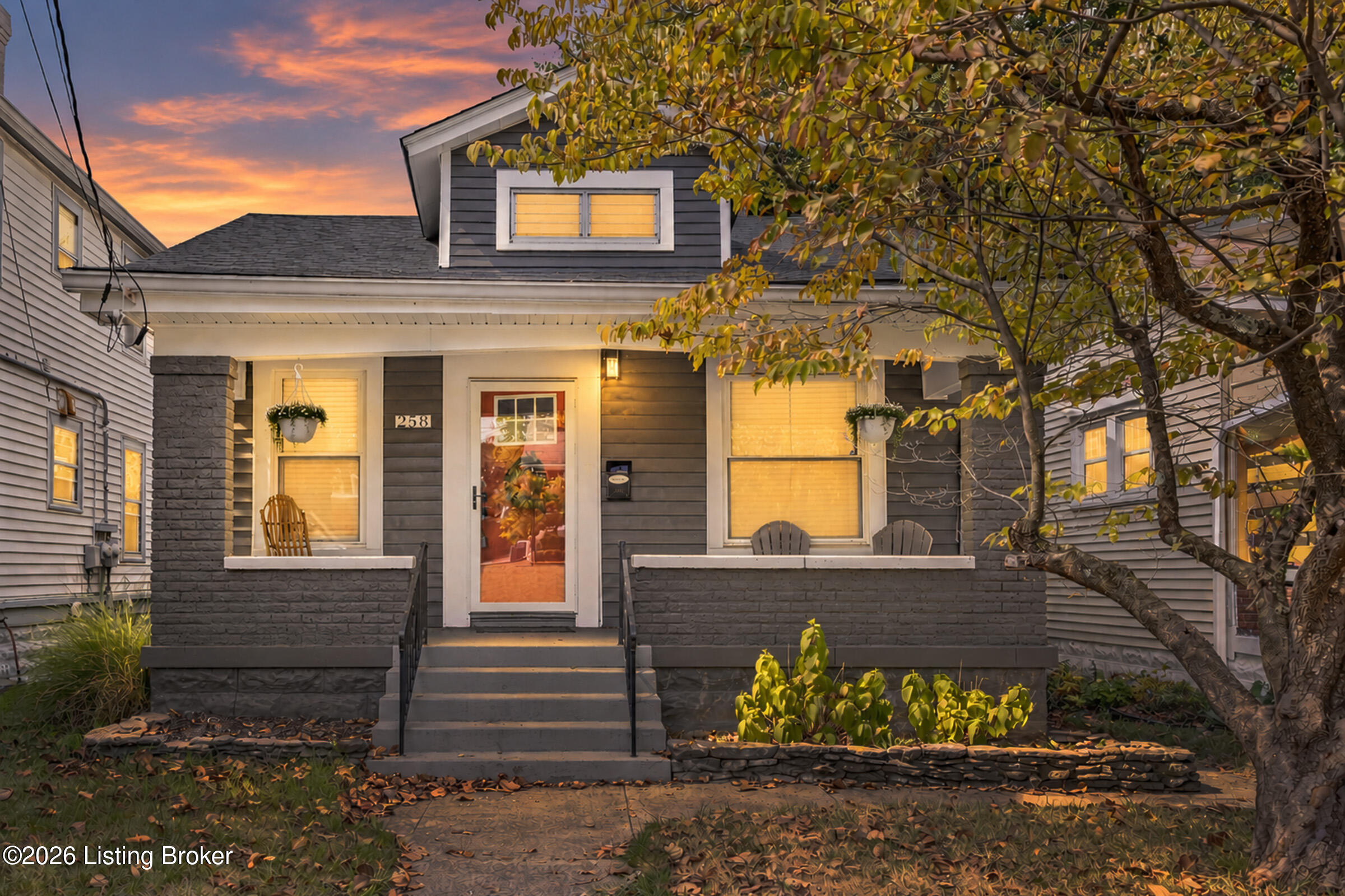 Gray house with a covered porch and stone pillars beneath a colorful autumn sunset.