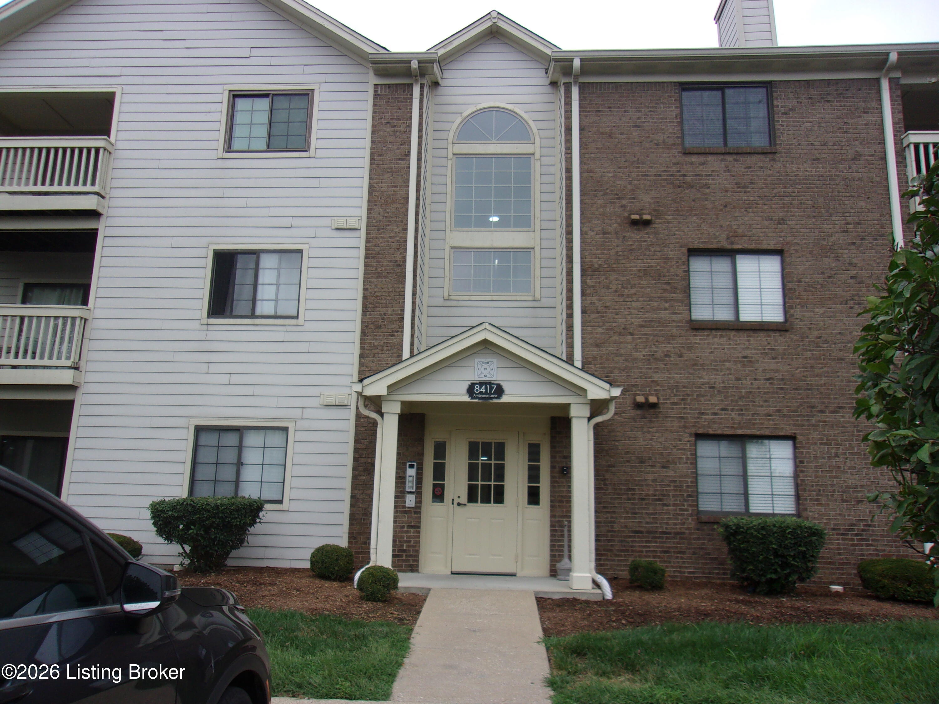 Apartment building entrance with a covered portico and tall arched window above.