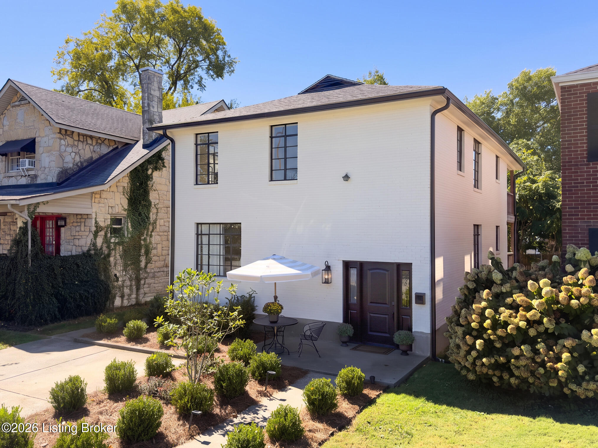 White two-story home with dark-framed windows, a courtyard patio, and flowering hydrangeas.