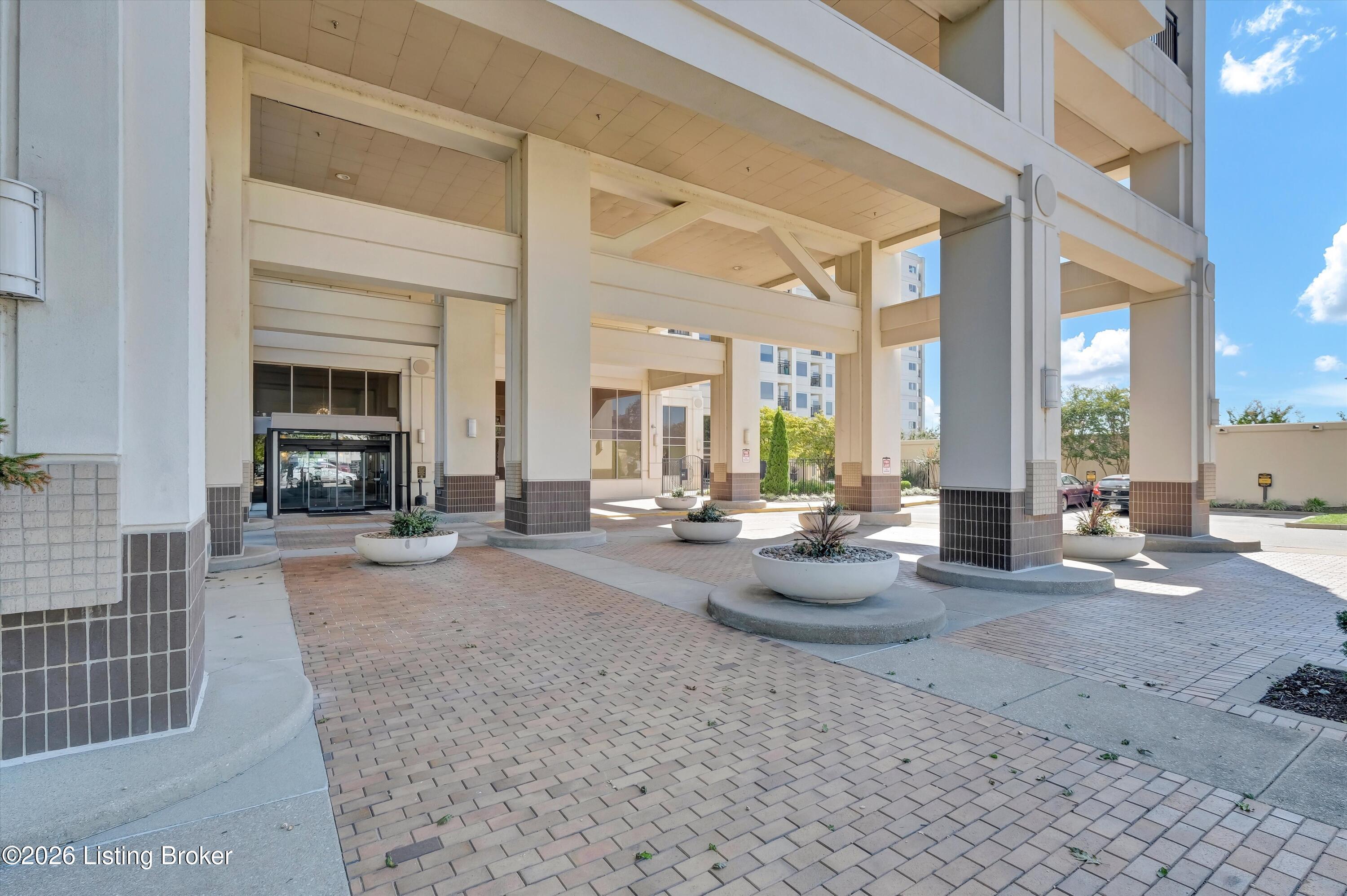 Modern building entrance beneath a covered porte cochere, with square columns and round planters.