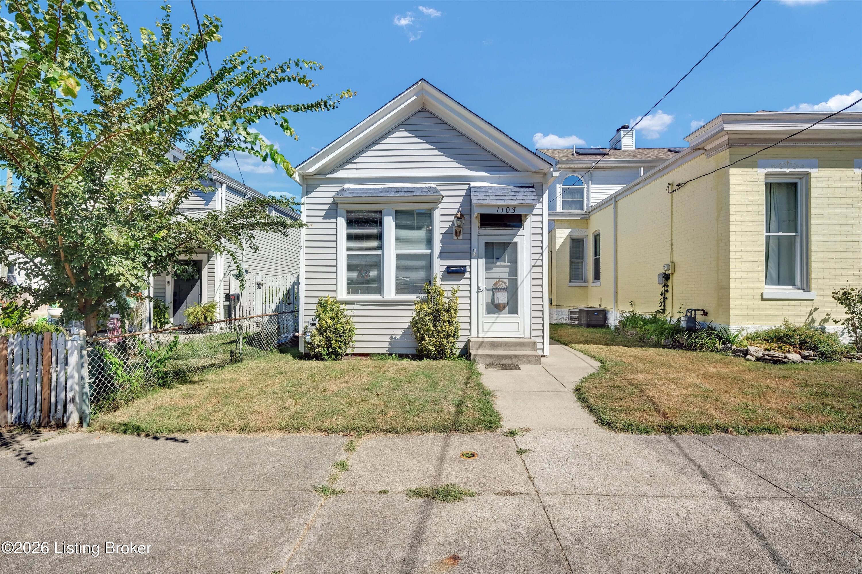 White-sided house numbered 1103 with a gabled roof and narrow front lawn.