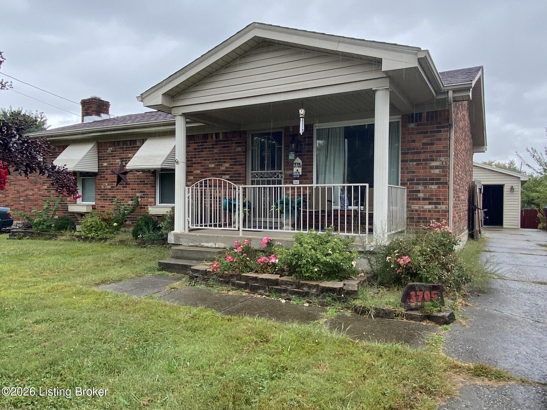 Brick ranch home with a covered front porch, white railing, and flower beds.