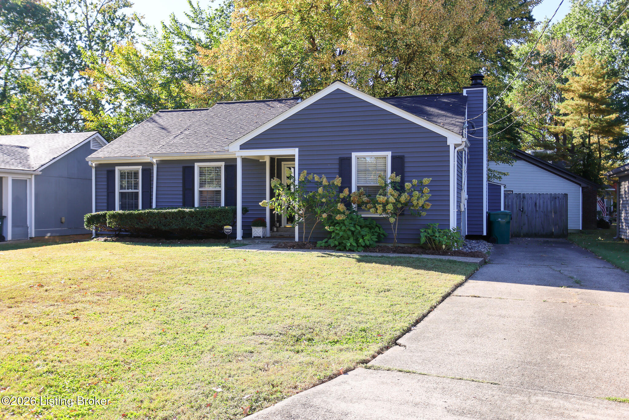 Blue single-story home with a covered porch, landscaped shrubs, and driveway.