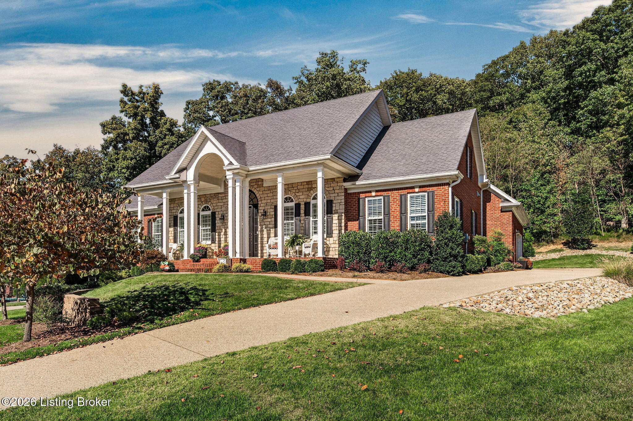 Two-story brick and stone home with a columned porch, landscaped lawn, and broad driveway.