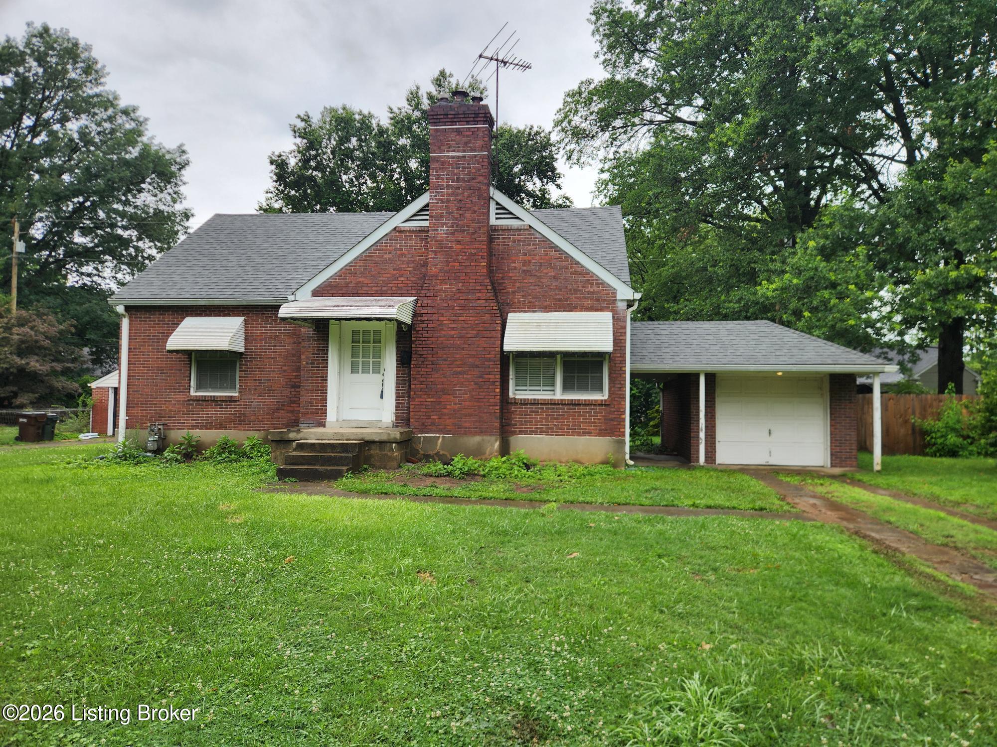 Red brick house with a prominent central chimney, attached garage, and broad green lawn.