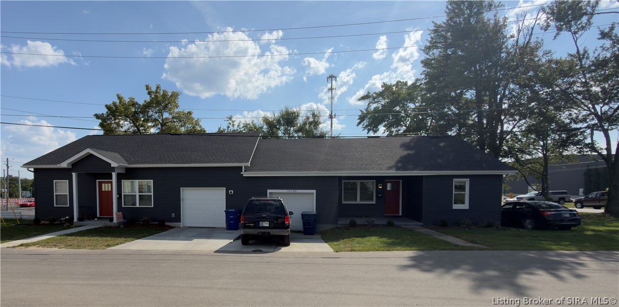 Long, single-story dark-sided building with red doors, white garage doors, and cars parked in front.