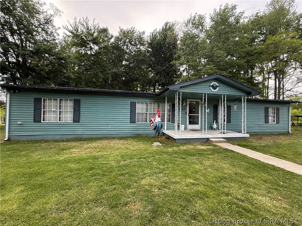 Single-story teal house with a covered porch, broad lawn, and rooster ornament by the walkway.