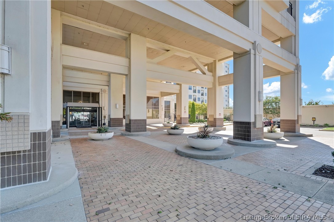 Building entrance with a covered drop-off area, broad columns, brick paving, and round planters.