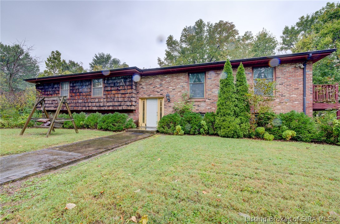 Single-story brick house with a wood-shingle facade, front lawn, walkway, and wooden swing.