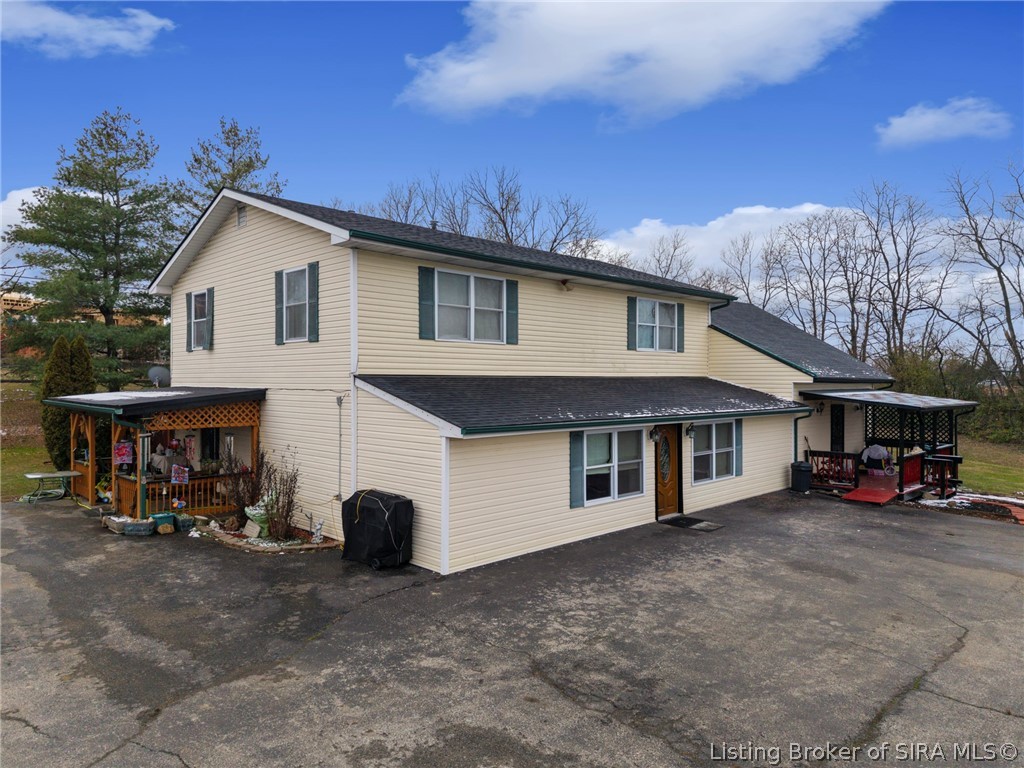 Two-story beige-sided house with dark green shutters, covered porches, and a broad asphalt driveway.