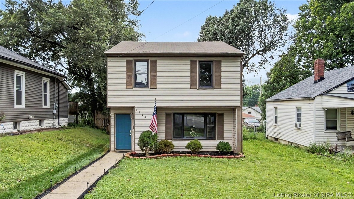 Two-story beige house with a blue front door, American flag, and walkway across the front lawn.