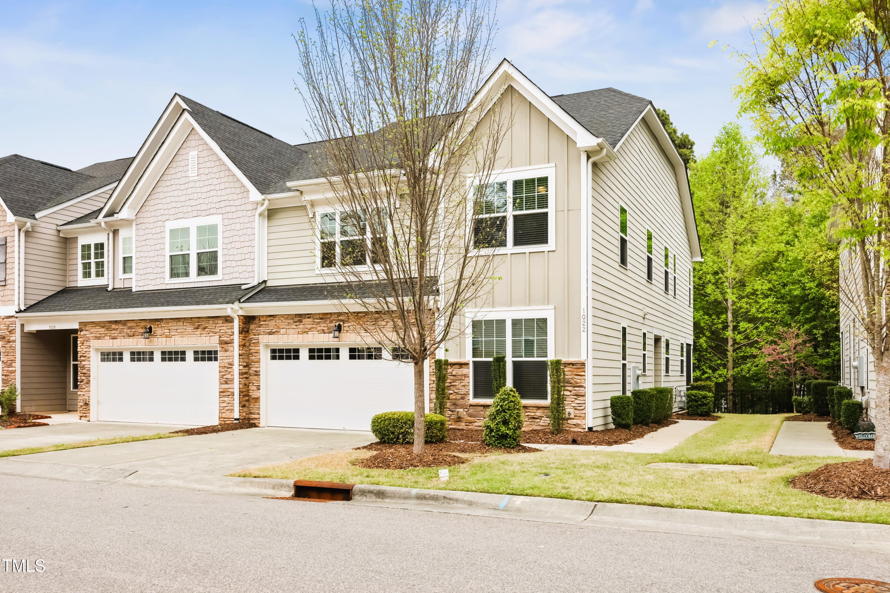 Attached two-story townhomes with stone veneer, white garage doors, and landscaped front lawns.