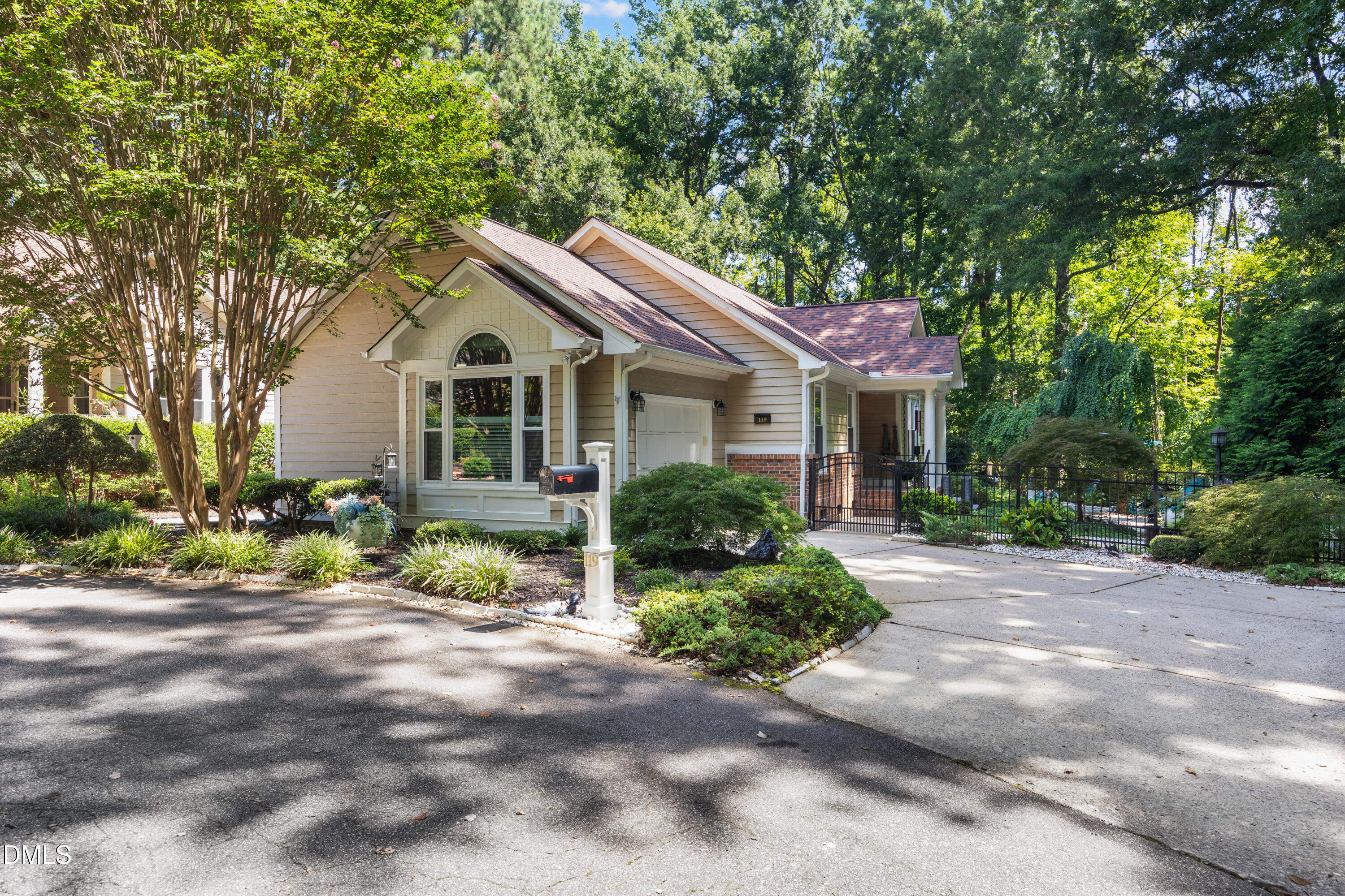 Beige home with an attached garage, landscaped yard, driveway, and mature trees.