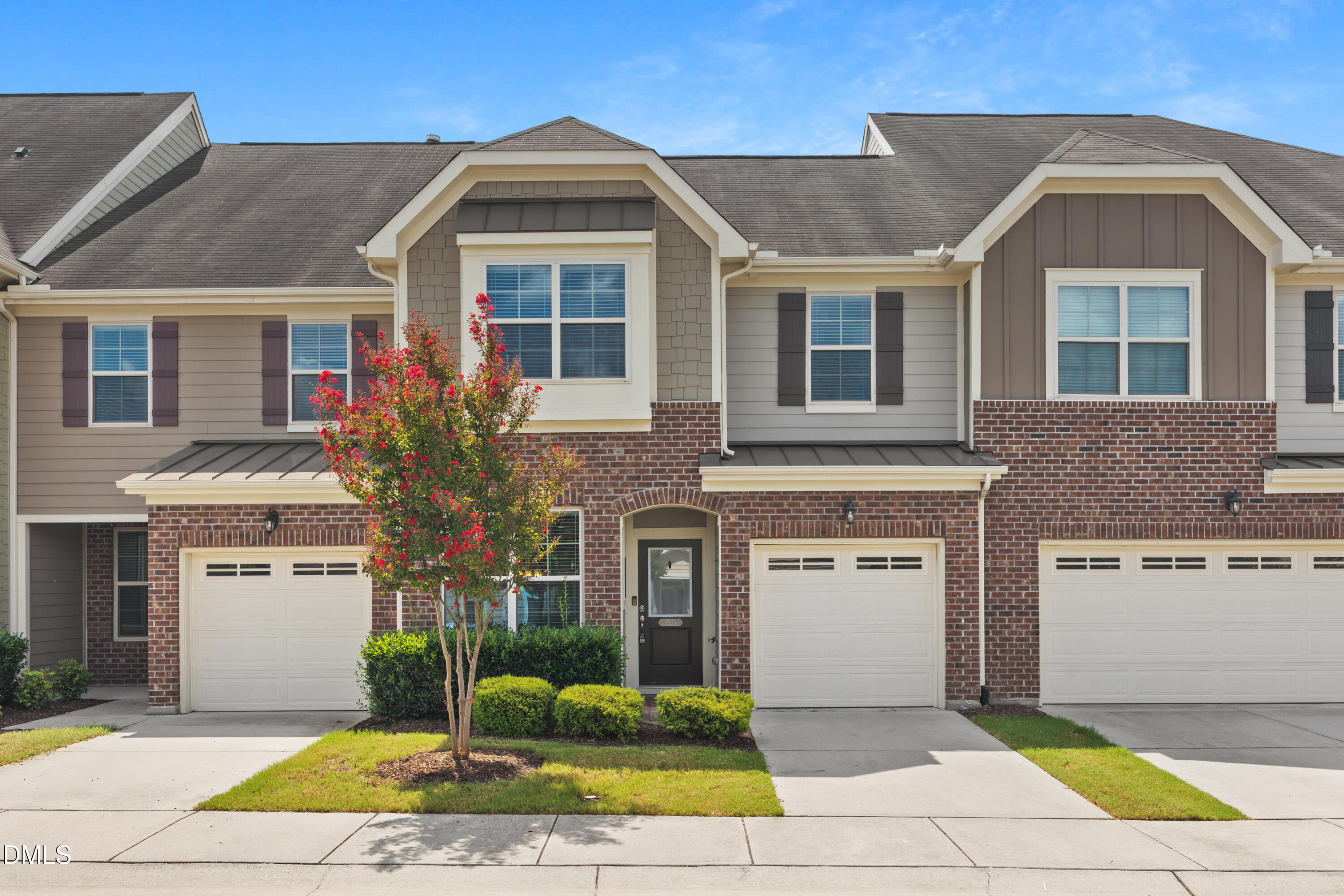 Two-story townhome with brick exterior, a one-car garage, and a red-flowering tree in front.