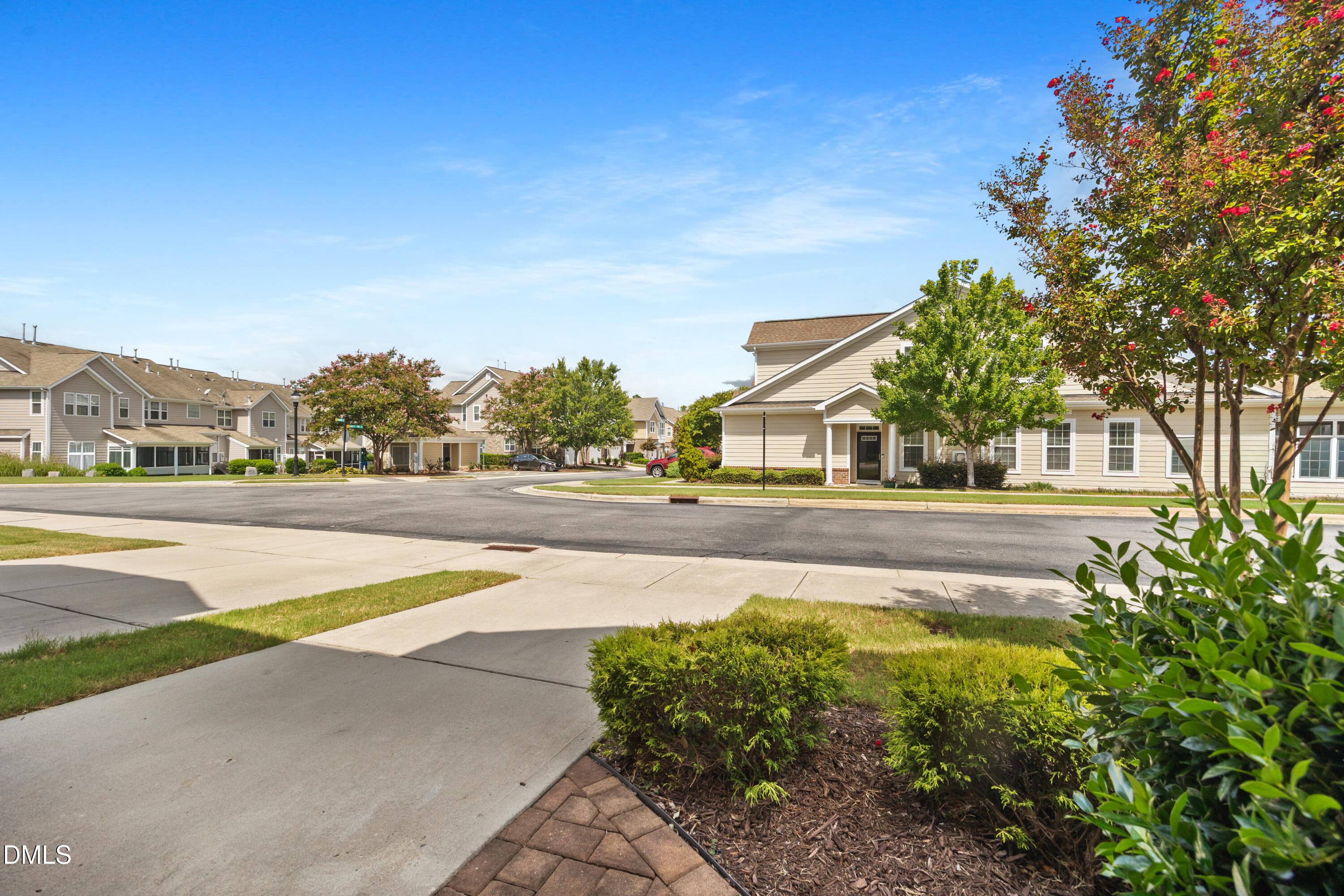 Beige homes along a landscaped residential street, framed by leafy trees and shrubs.