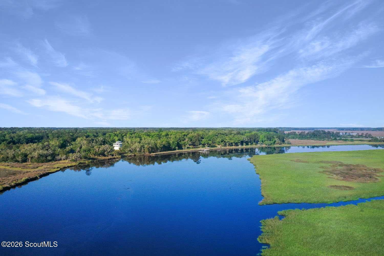 Aerial view of a waterway edged by marsh grass and woods, with a dock along the shoreline.