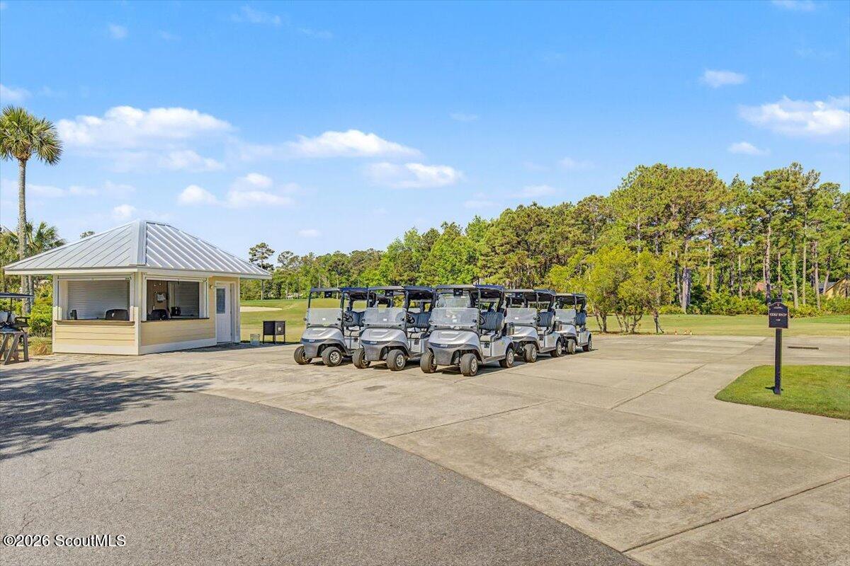 Golf carts lined up beside a small covered booth at a golf course.