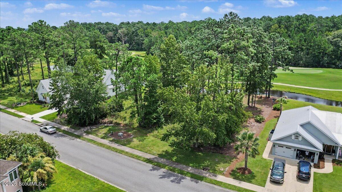 Aerial view of a wooded vacant lot beside a street, with a golf course and pond nearby.