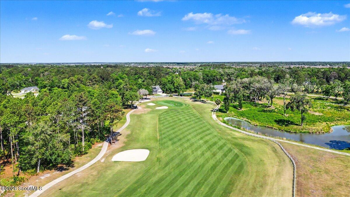 Aerial golf course view with striped fairway, sand bunkers, and a pond.