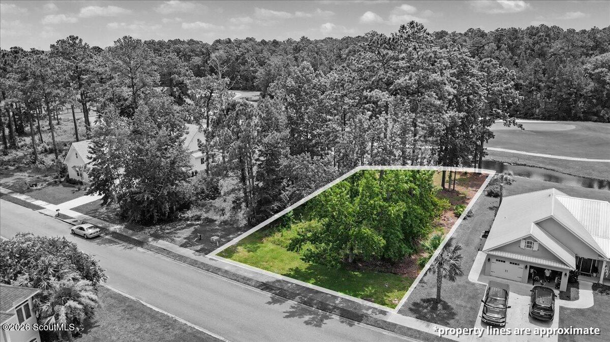 Aerial view of a wooded lot outlined beside a street, with a golf course and homes nearby.