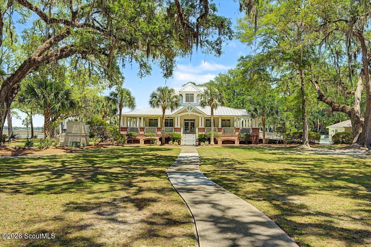 Raised building with a covered porch and brick supports, framed by mature trees and a curved walkway.