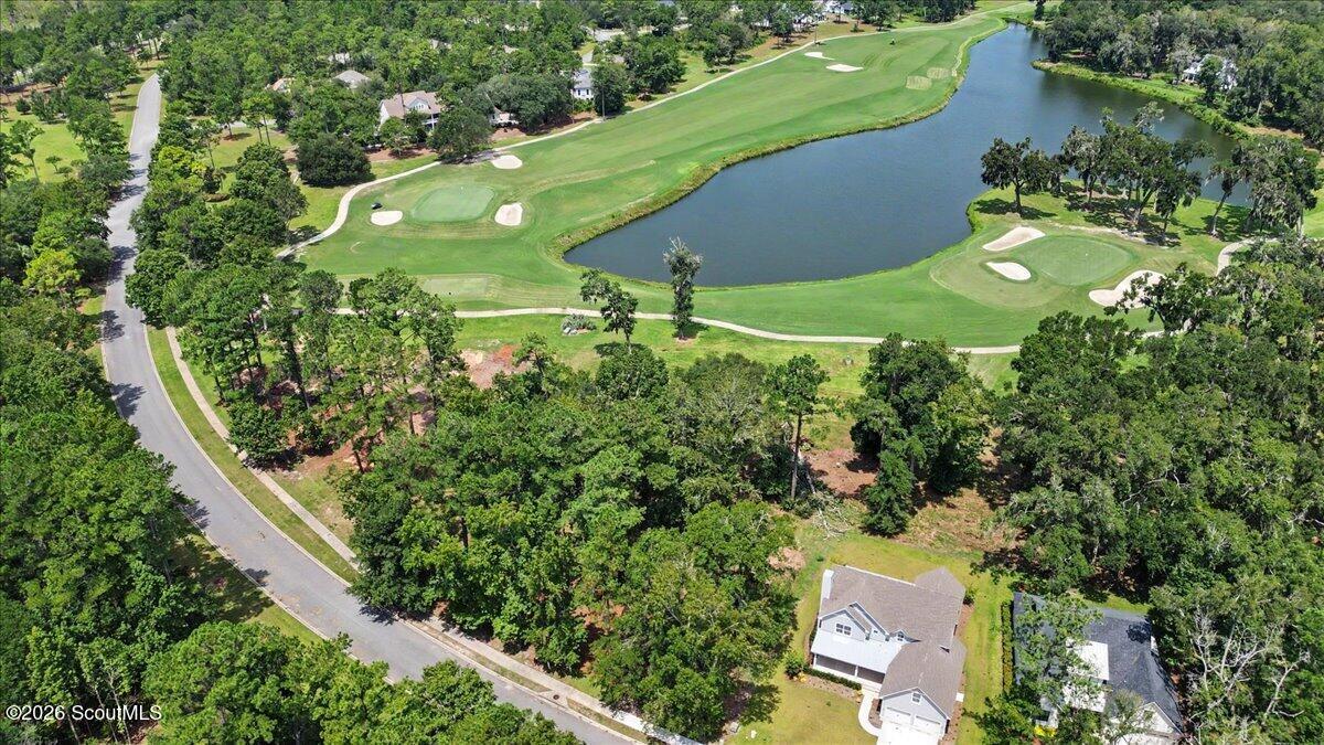 Aerial view of a wooded lot beside a golf course pond and nearby homes.
