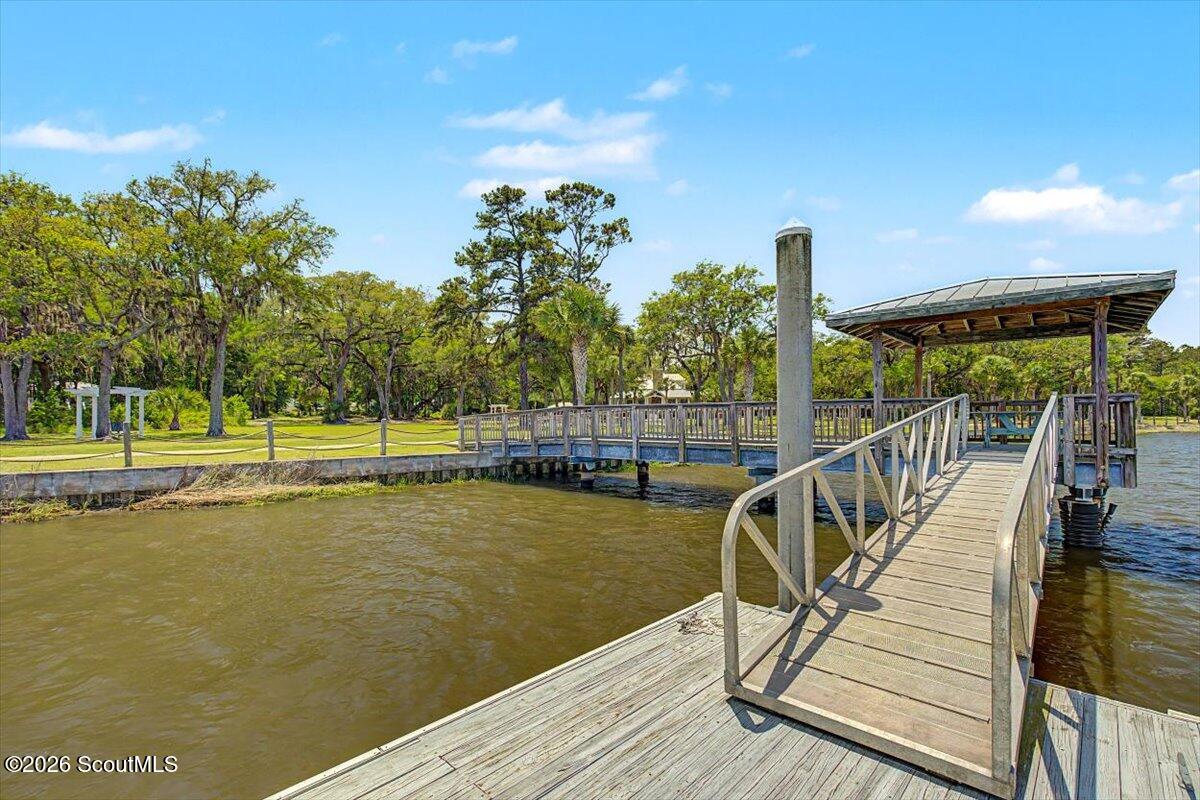 Waterfront dock with a ramp leading to a covered pavilion beside a tree-lined shore.