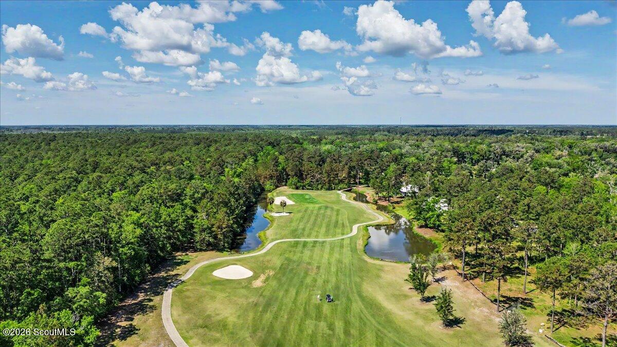 Aerial golf course fairway with a winding path, sand bunker, ponds, and surrounding woodland.
