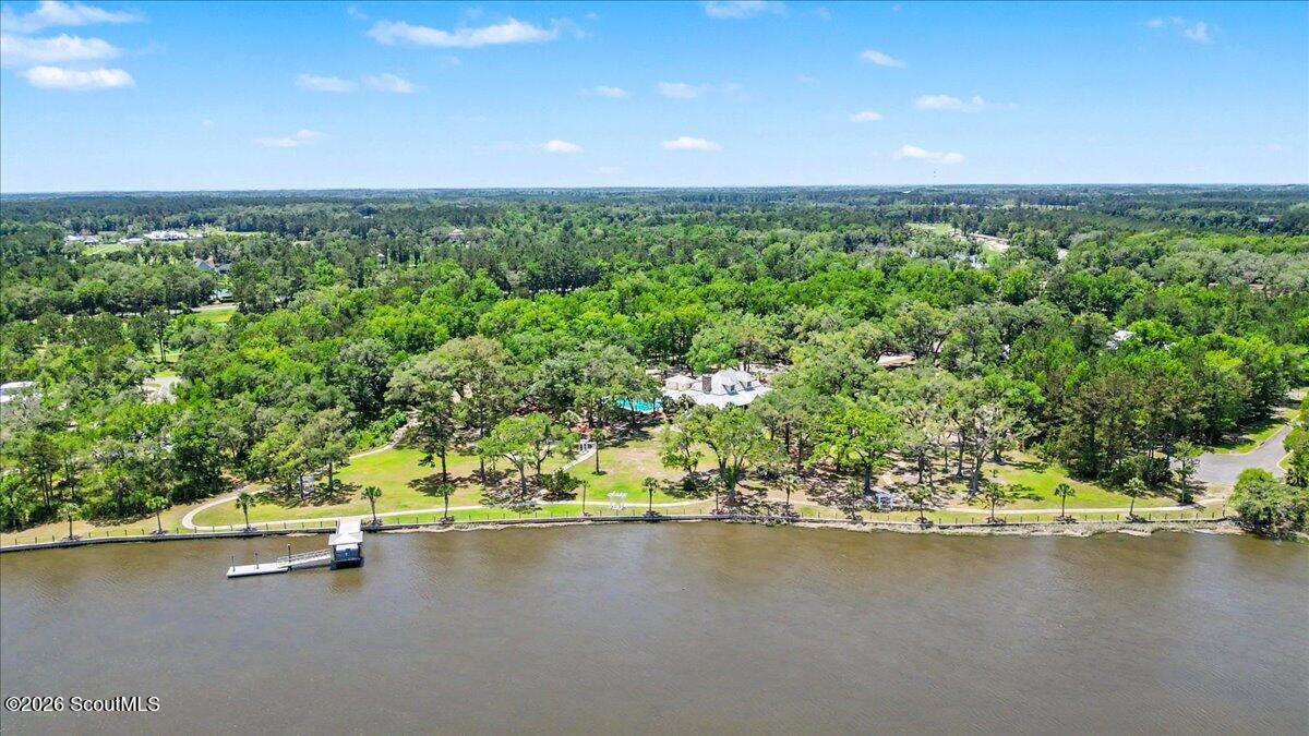 Aerial waterfront view with a dock, tree-lined shoreline, and wooded grounds.