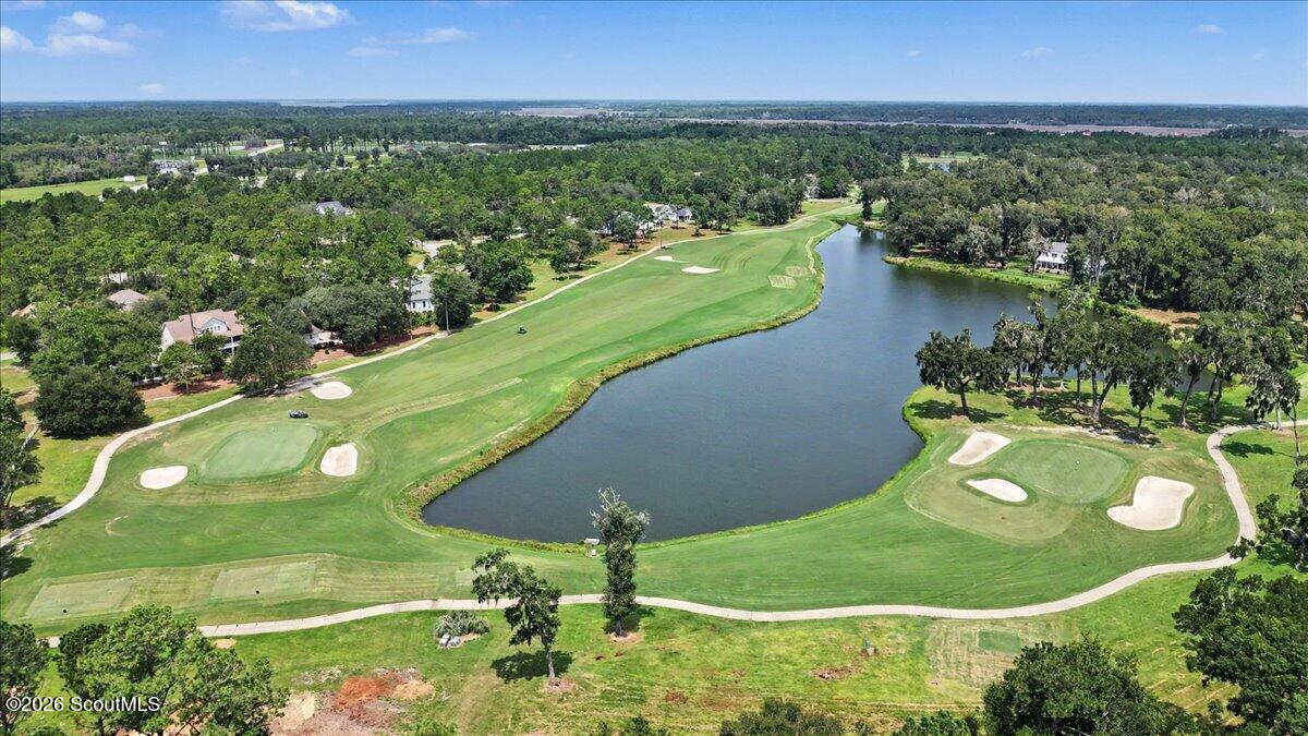Aerial view of a golf course and pond, with greens, sand bunkers, and wooded homes.