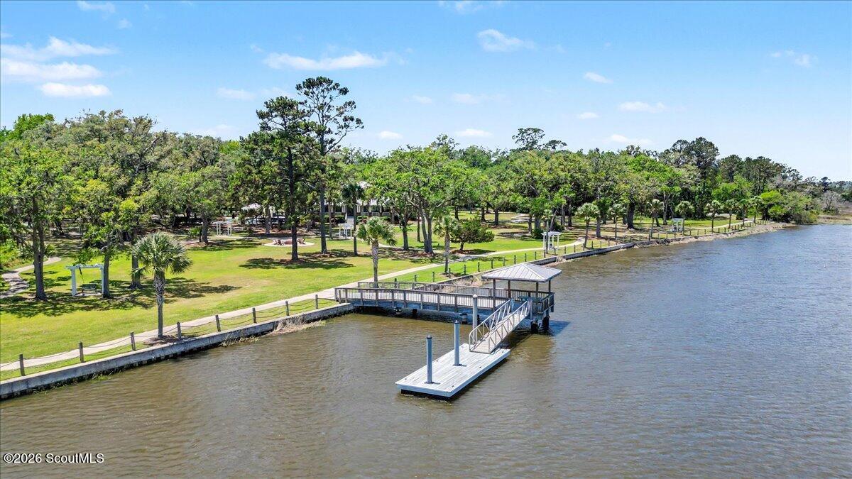 Waterfront lawn and mature trees beside a long dock extending into the water.