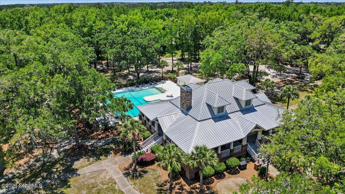 Aerial view of a gray-roofed home and swimming pool surrounded by dense woodland.