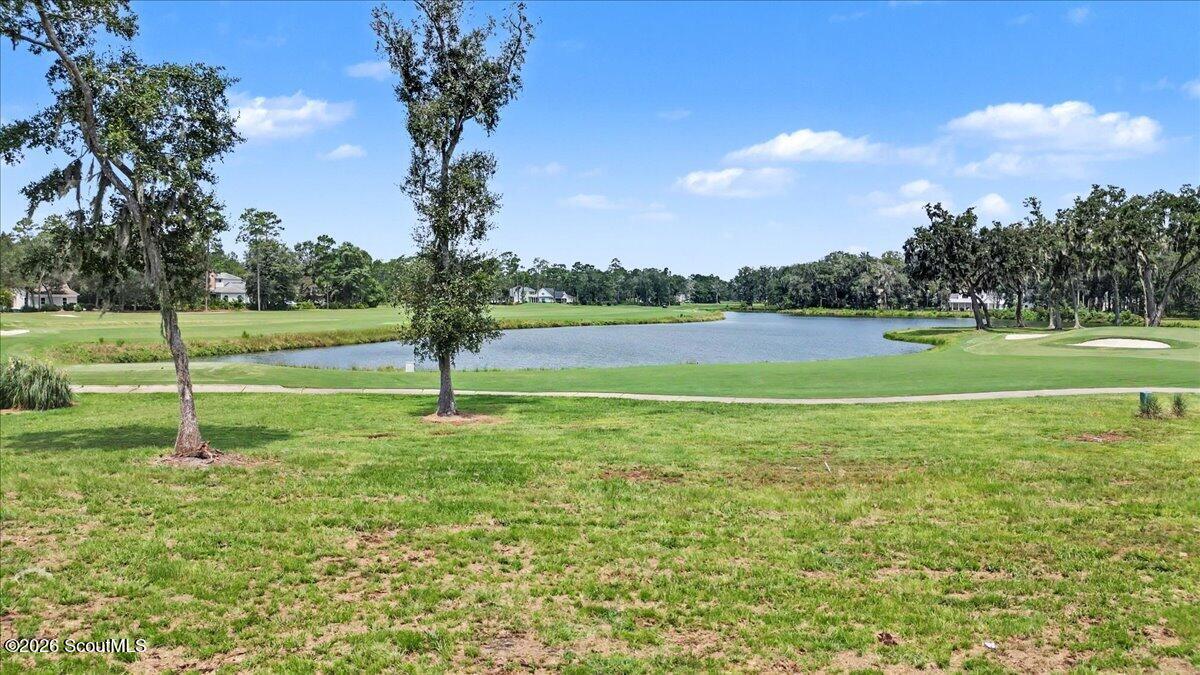 Vacant grassy lot overlooking a pond and golf course, with mature trees.