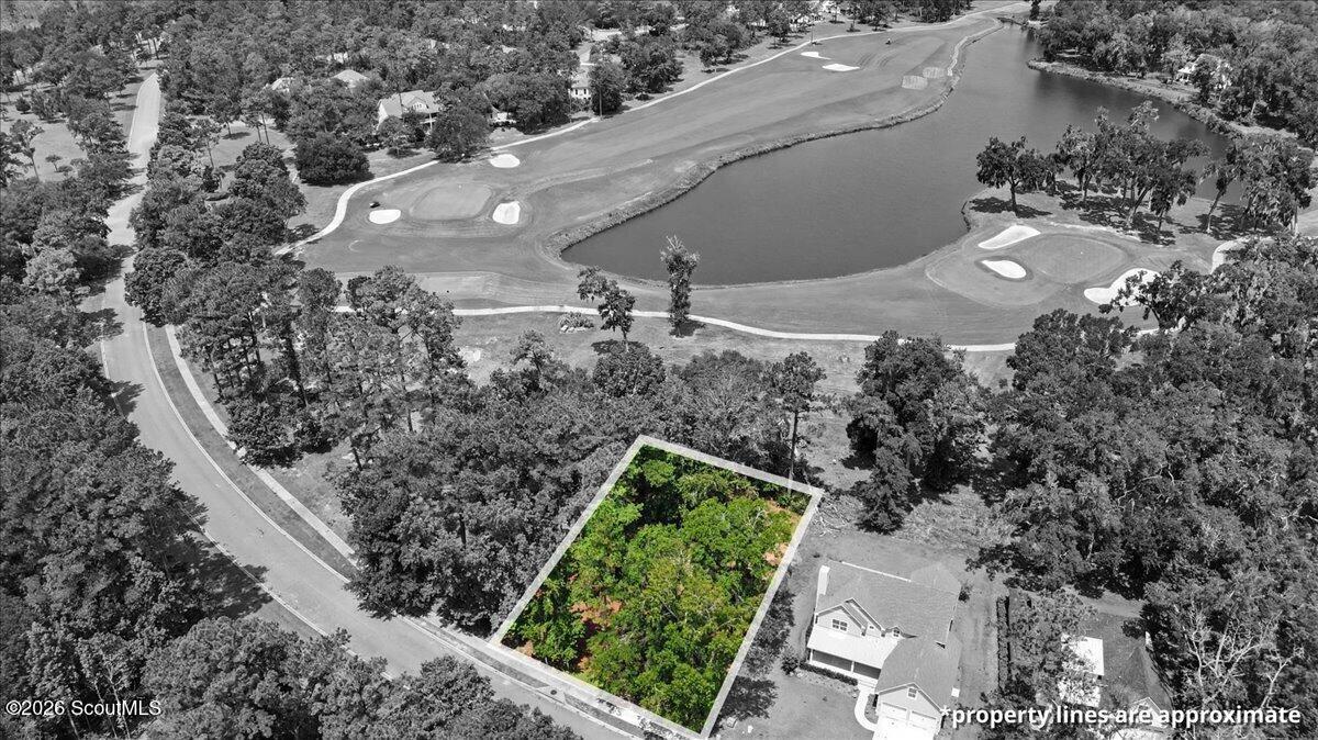 Aerial view of a wooded vacant lot beside a golf course and pond.