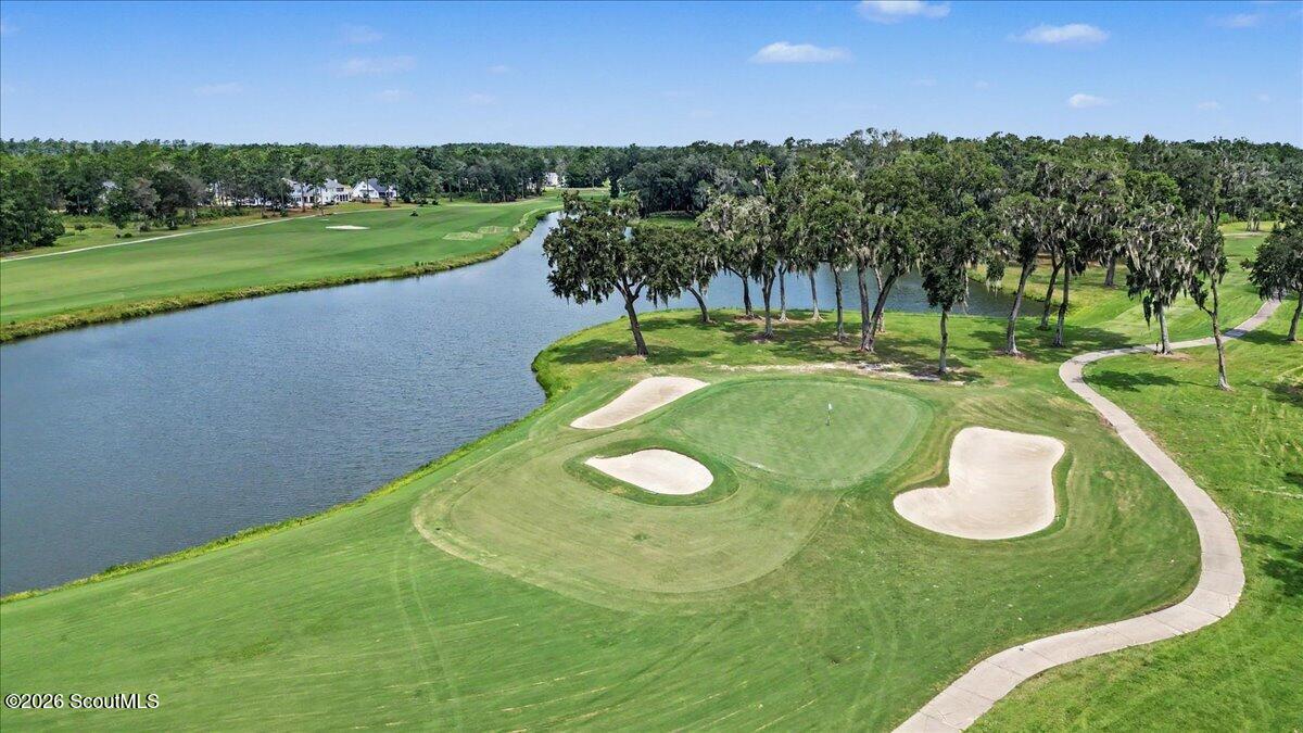 Aerial view of a golf green with sand bunkers beside a waterway and tree-lined path.