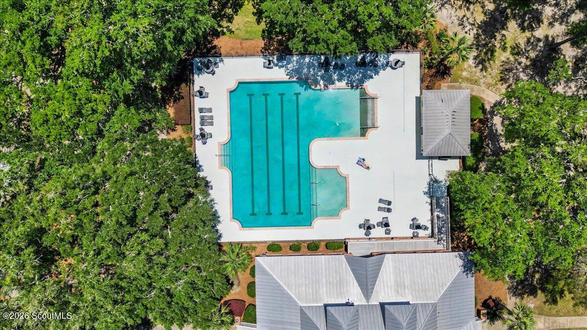 Aerial view of a lap pool and white deck surrounded by trees, with lounge chairs and a pavilion.