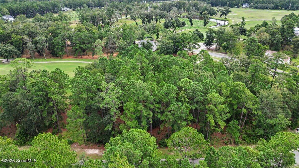 Aerial view of a wooded vacant lot beside a golf course.
