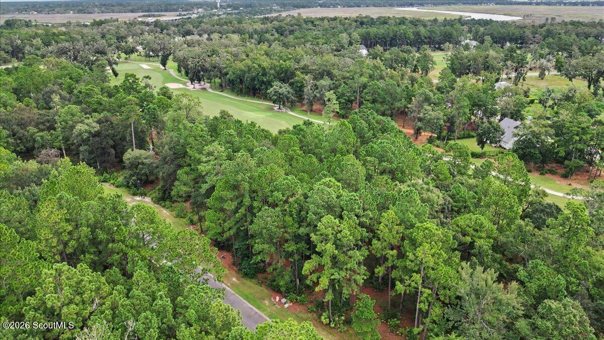 Aerial view of a wooded lot beside a golf course fairway and nearby homes.