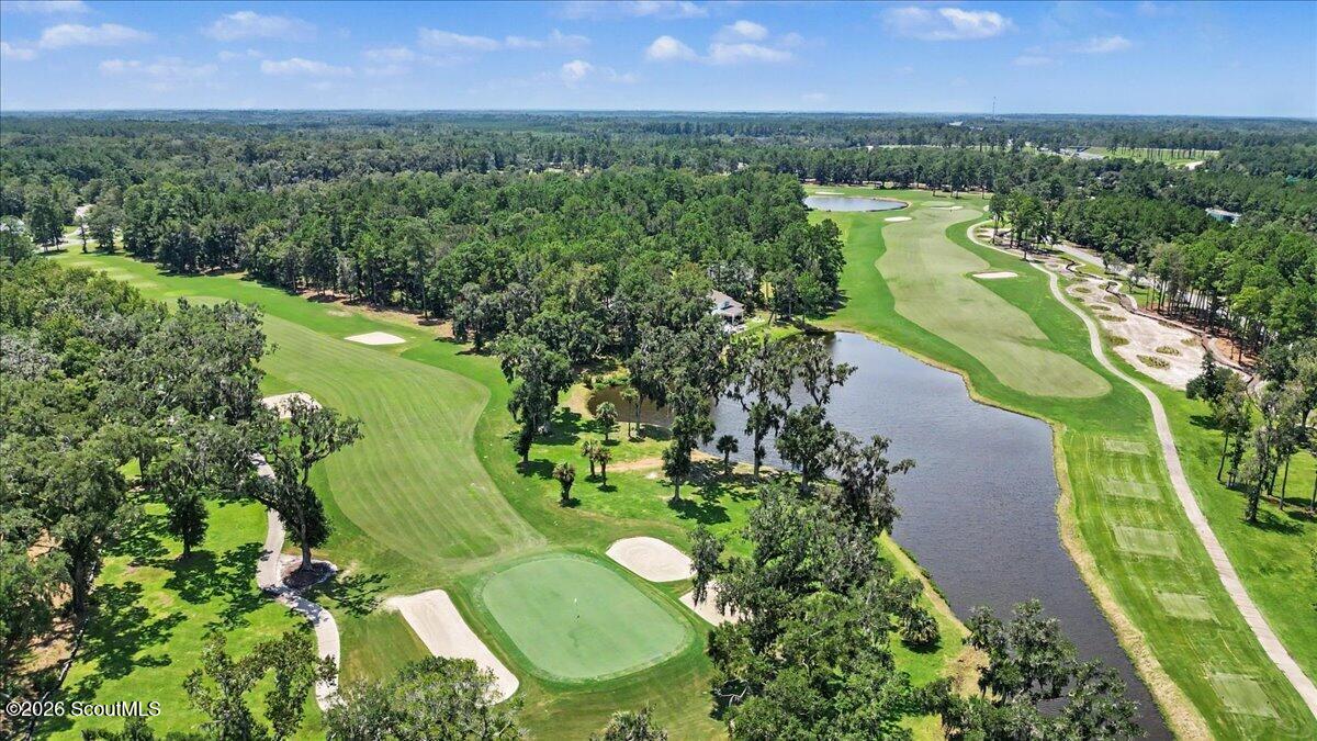 Aerial view of a golf course with winding fairways, bunkers, a pond, and surrounding trees.