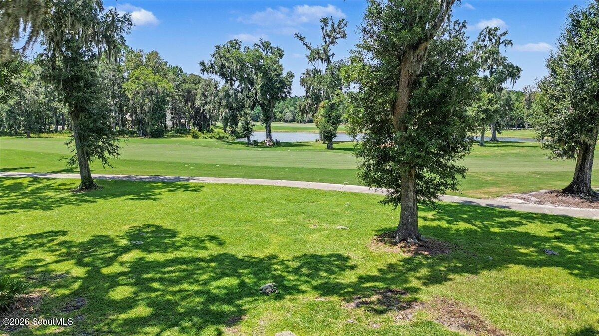 Golf course view with mature trees, a paved cart path, and a pond beyond the green.