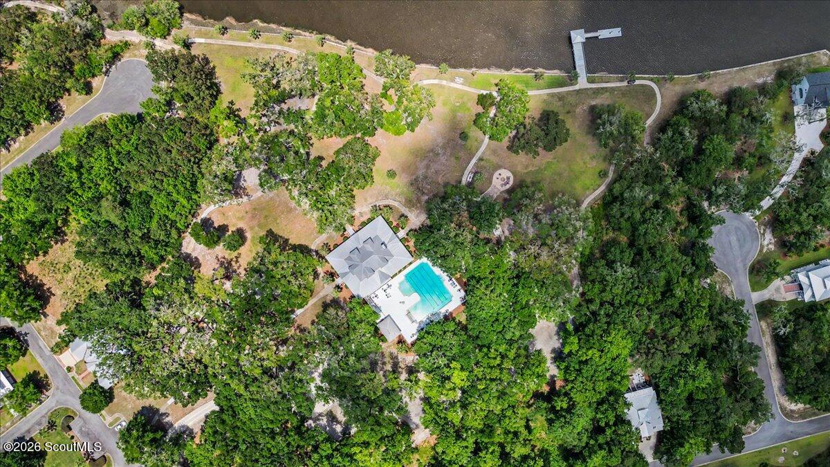 Aerial view of a wooded home beside the water, with a swimming pool and dock.