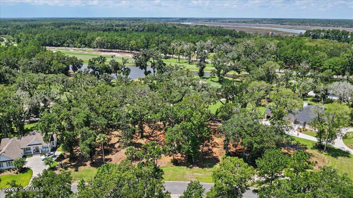 Wooded vacant lot beside a residential road, with a golf course and pond nearby.