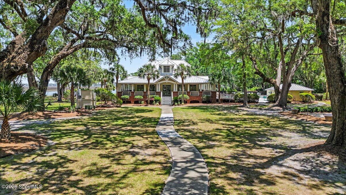 A low brick-and-siding building with a wraparound porch, framed by moss-draped oaks and a curved walkway.